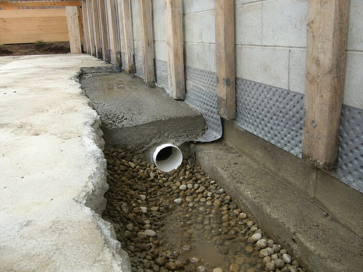Basement perimeter drain trench with drain pipe outlet and stone bedding in Pittsburgh