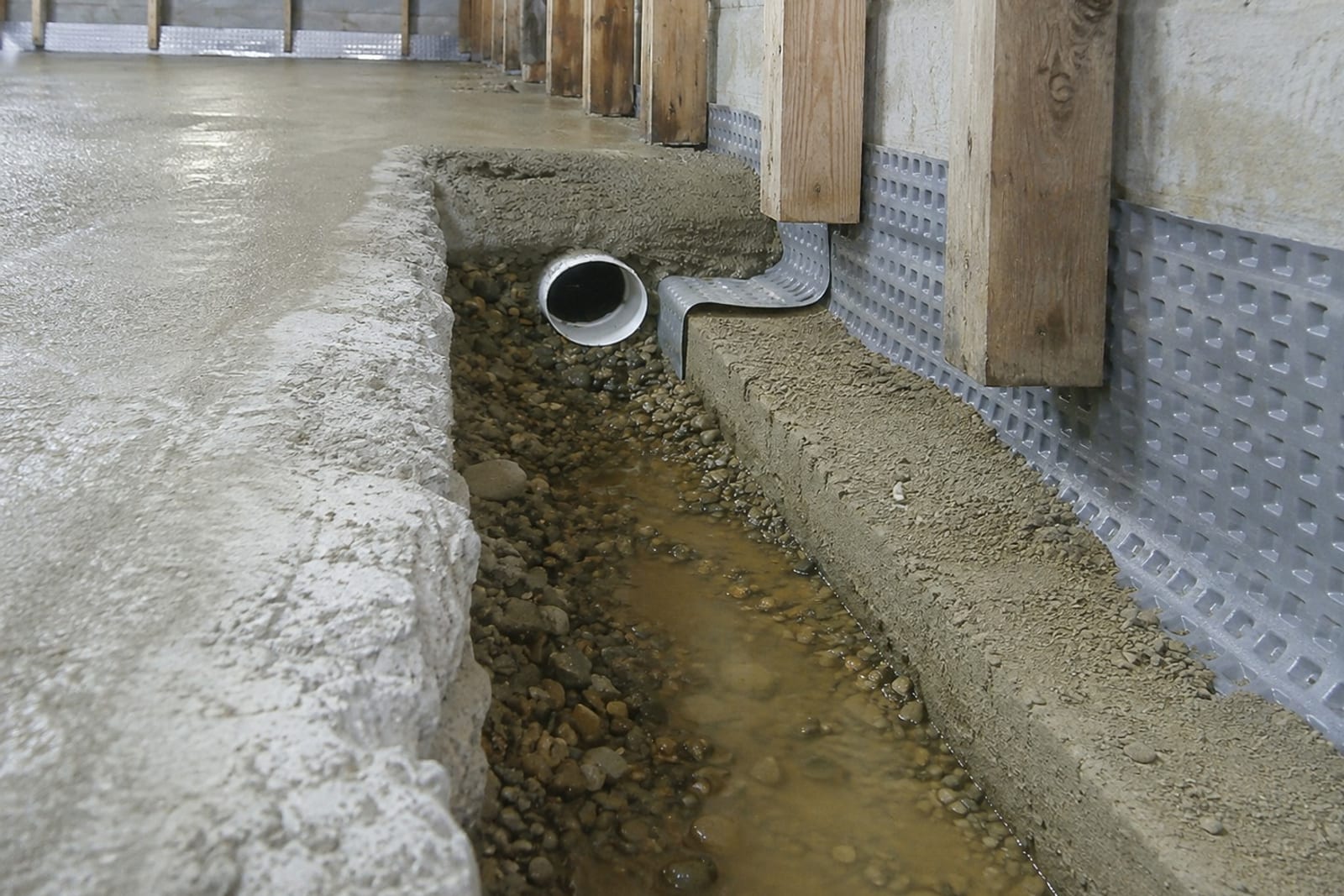 Interior French drain channel cut around a basement perimeter with perforated pipe and washed stone