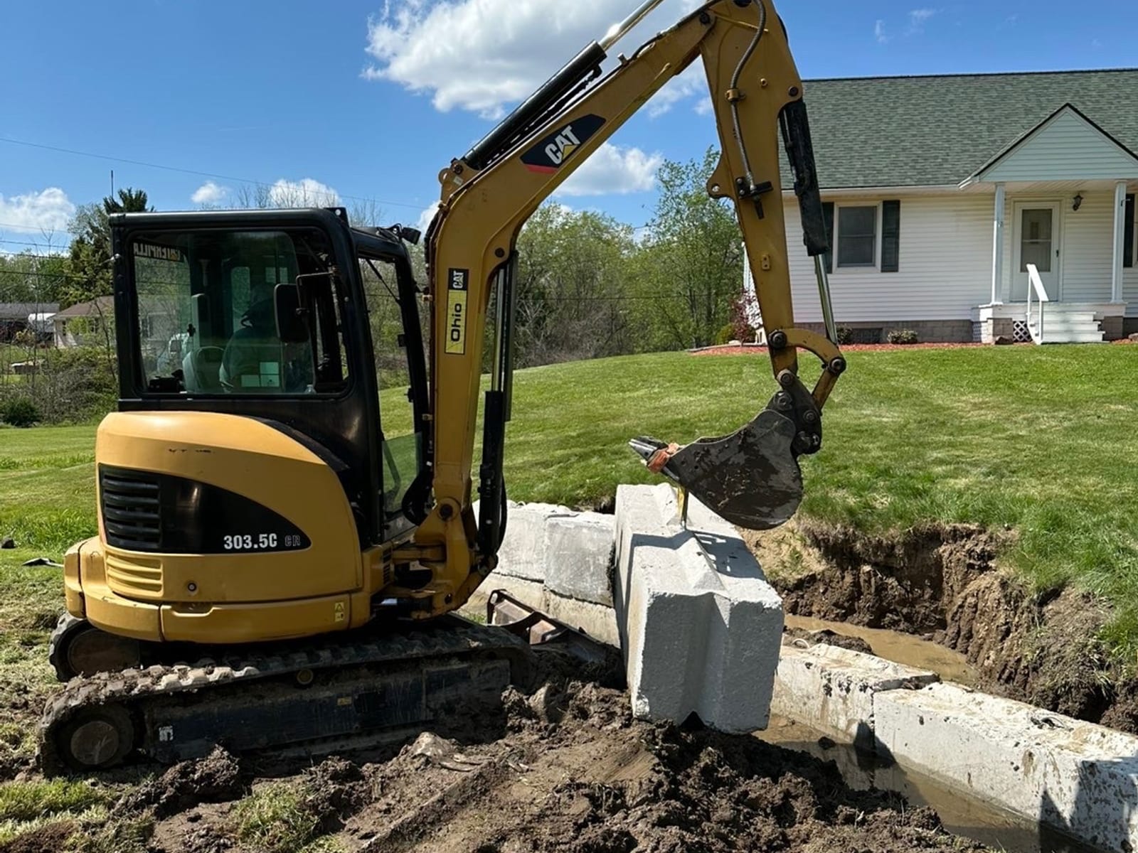 Mini excavator setting concrete blocks in a residential drainage trench in Pittsburgh